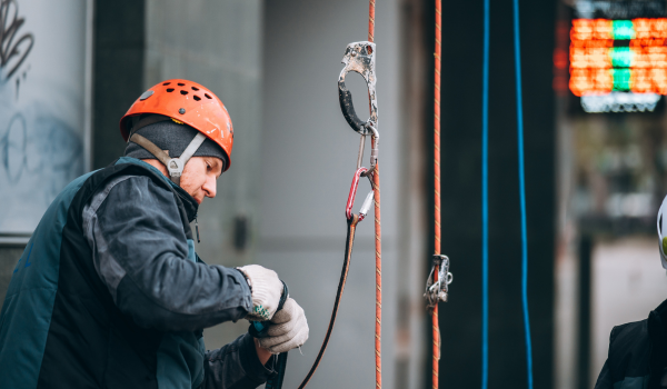 Profissional preparando equipamento de acesso por corda para alpinismo industrial com segurança