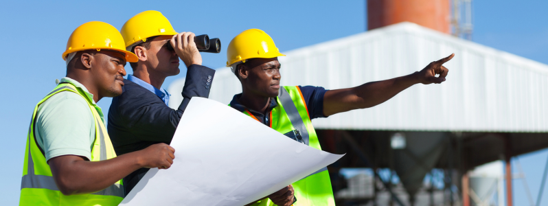 Engenheiros com capacetes analisando planta de projeto industrial em área fabril