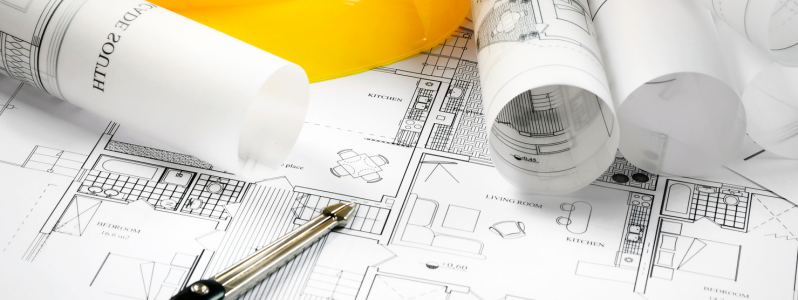 Plantas e projetos de arquitetura industrial com capacete de segurança sobre a mesa.