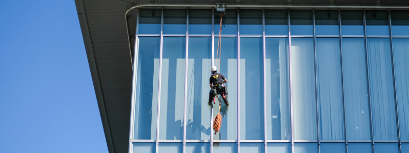 Profissional realizando trabalho em altura com linha de vida em fachada industrial, representando os serviços de segurança estrutural da HR Soluções.
